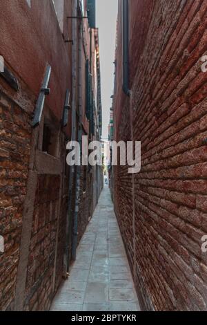 Wirklich schmale Gasse mit Ziegelwänden an den Seiten in Venedig Stockfoto