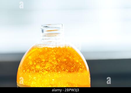 Flüssige Seife von oranger Farbe in einer transparenten Flasche auf einem hellen Hintergrund, flüssige Seife mit Blasen Stockfoto