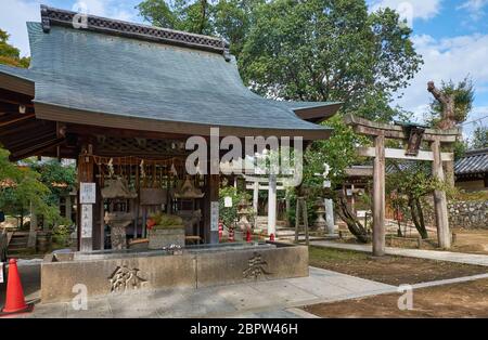 KYOTO, JAPAN - 17. OKTOBER 2019: Wasserwaschung Pavillon für zeremonielle Reinigung (Chozuya oder temizuya) mit dem steinernen Torii-Tor im Hintergrund Stockfoto