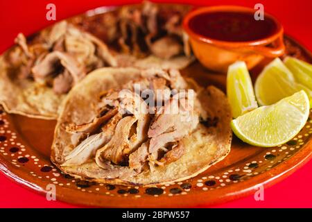 Mexican Carnitas Tacos ist ein traditioneller Schweinetaco mit Maissortilla und Sauce in Mexiko Stadt auf rotem Hintergrund Stockfoto