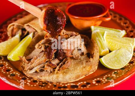 Mexican Carnitas Tacos ist ein traditioneller Schweinetaco mit Maissortilla und Sauce in Mexiko Stadt auf rotem Hintergrund Stockfoto