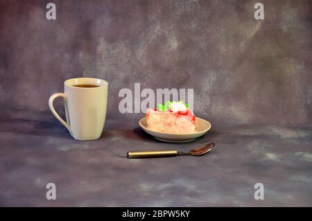 Weißer hoher Becher mit schwarzem Kaffee und einem Teller mit einem dreieckigen Kekskuchen in roter Glasur auf einem grauen abstrakten Hintergrund. Nahaufnahme. Stockfoto