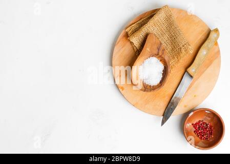 Kleine Holzschalen mit natürlichem Salz und rotem Chili auf Holzbrett und Messer zur Zubereitung von hausgemachten frischen Speisen auf hellgrauem Marmor Stockfoto