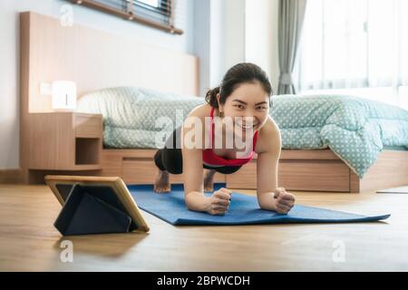 Asiatische Frau Yoga von zu Hause aus mit Laptop, wenn Covid19 Ausbruch und Lockdown, gesunde oder Meditation Übung, Training zu Hause, Coronavirus Pfanne Stockfoto