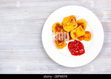 Draufsicht auf gebratene Hühnernuggets mit Ketchup auf weißem Teller auf grauem Holzbrett Stockfoto