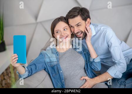 Junge schwangere Frau macht Selfie mit ihrem Mann und lächelt Stockfoto