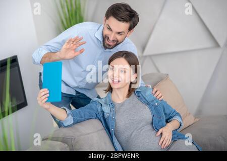 Junge schwangere Frau und ihr Mann Video im Chat mit Freunden Stockfoto