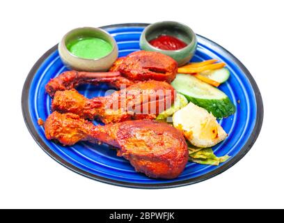 Indische Küche: Gekochtes Tandoori-Huhn (in Joghurt und Gewürzen marinierte, in Tandoor geröstete, würzige Hähnchenschenkel) mit Saucen auf blauer Keramikplatte Stockfoto