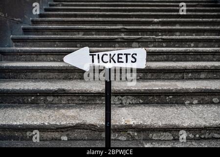 Ein Pfeil mit dem Wort 'Tickets' weist auf den Weg zu einem Ticketschalter vor einer Steintreppe. Stockfoto