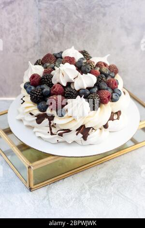 Baiser Pawlova mit frischer reifer Himbeere, Brombeere und Heidelbeere und Schlagsahne auf grauem Hintergrund. Stockfoto