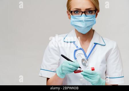 Arzt Krankenschwester Frau trägt Schutzmaske und Handschuhe - Marke mit Stift auf Virus Blut Teströhrchen Stockfoto