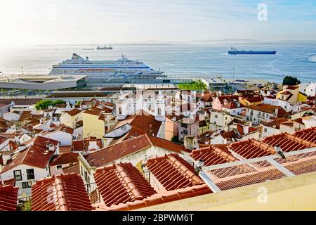 Blick auf ein Kreuzfahrtschiff im Fluss Tejo hinter den Dächern des Stadtteils Alfama von Lissabon vom Miradouro de Santa Luzia aus gesehen Stockfoto