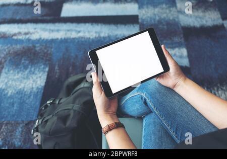 Mockup Bild von einer Frau mit und über schwarze Tablet-PC mit leeren weißen Bildschirm, während im Flughafen sitzen Stockfoto