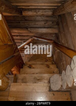 Eine Treppe mit spiralförmigem Abstieg, gefaltete Holztreppen, mit einem dunkelbraunen Lack eines traditionellen Designs in einem Haus mit Blockhaus bedeckt. Stockfoto