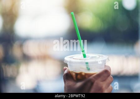 Eine Hand, die ein Plastikglas Eiskaffee mit Stroh hält Stockfoto