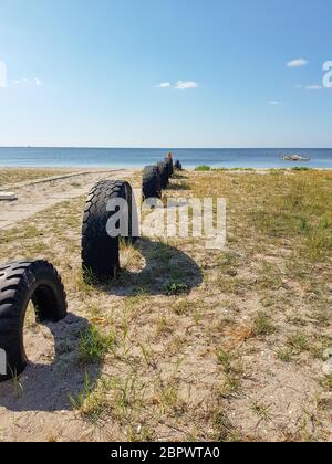 Autoreifen, die halb im Sand auf einem Strand mit Gras vergraben sind. Stockfoto