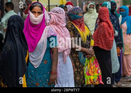 Indische Frauen warten auf kostenlose Nahrung in der Region Mustafabad, die kürzlich von Unruhen betroffen war, als das Land seine Lockdown-Beschränkung am 14. Mai 2020 in Neu-Delhi, Indien, lockert. Die Region Mustafabad gehörte zu den am schlimmsten betroffenen Gebieten, als im Februar in Indiens Hauptstadt Unruhen ausbrachen, weil ein umstrittenes Gesetz zur Änderung der Staatsbürgerschaft von der Regierung der Bharatiya Janata Partei verabschiedet wurde. Mehrere Familien, die aufgrund von Brandstiftung durch Randalierer obdachlos waren, kümmern sich nun um sich selbst inmitten einer landesweiten Lockdown, die von der Regierung auferlegt wurde, um die Ausbreitung des Coronavirus im Land einzudämmen. Zoll Stockfoto