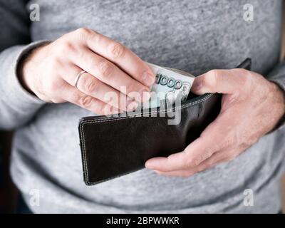Hände nehmen Sie russische Rubel aus der Brieftasche. Nahaufnahme auf die Hände eines Menschen, wie er ist, eine Banknote aus seiner Brieftasche Stockfoto