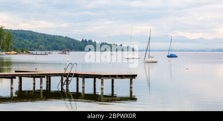 Blick auf den Ammersee mit Holzsteg, Segelbooten und - weit in der Ferne - den alpen (Wettersteingebirge). Panoramafarma. Stockfoto