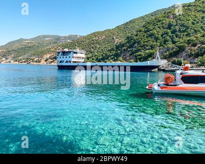 Ein Pier am Fuße des Berges Athos in Griechenland. Klares Meerwasser, ein trockenes Frachtschiff, ein kleines Boot und ein Wald im Hintergrund Stockfoto