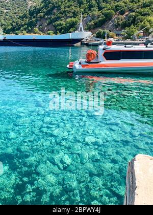Ein Pier am Fuße des Berges Athos in Griechenland. Klares Meerwasser, ein trockenes Frachtschiff, ein kleines Boot und ein Wald im Hintergrund Stockfoto