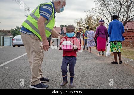 Johannesburg, Südafrika. Mai 2020. Ein Kind, das eine Gesichtsmaske trägt, bekommt in Johannesburg, Südafrika, 19. Mai 2020 Gemeinschaftskost. Am Dienstag hat Südafrika 17,200 bestätigte COVID-19-Fälle verzeichnet, gegenüber Montag um 767, und 312 Todesfälle, was einem Anstieg von 26. Kredit: Yeshiel/Xinhua/Alamy Live News Stockfoto