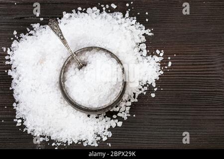 Blick von oben auf die Vintage silver Salz mit Löffel mit grobkörnigem Meersalz und Haufen das Salz auf Dunkelbraun Holzbrett Stockfoto