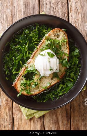 Portugiesische Knoblauch und Cilantro Brotsuppe Acorda serviert mit pochiertem Ei aus nächster Nähe in einem Teller auf dem Tisch. Vertikale Ansicht von oben Stockfoto