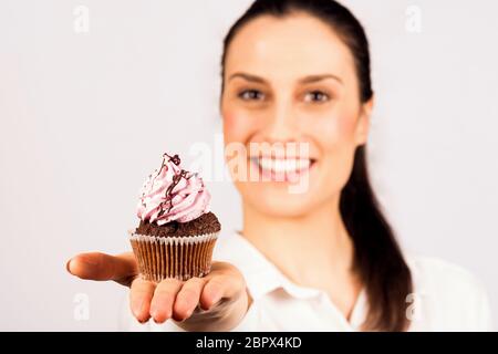 Die schöne junge lächelnde Frau hält einen süßen Cupcake in der Hand und präsentiert sich auf weißem Hintergrund. Stockfoto