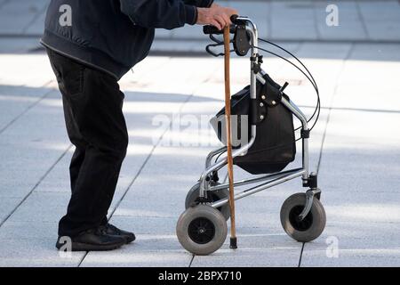 Ein älterer Mann benutzt eine Gehhilfe und einen Gehstock auf einer Straße in Großbritannien. Stockfoto