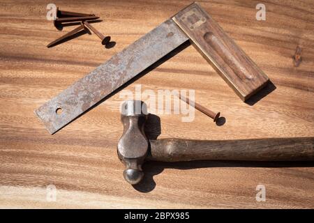 Ein alter Kugelhammerschlag, ein Messwerkzeug und alte rostige Nägel, die auf einer Holzplatte liegen. Vintage Retro Tischlerei Werkzeuge, diy Stockfoto