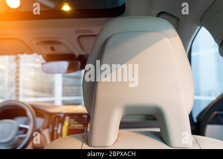 Nahaufnahme der Kopfstütze des Autositzes. Weißes Lederinterieur eines neuen modernen Autos, Abendsonne durch das Fenster. Stockfoto
