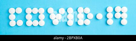 Inschrift COVID-19 aus weißen medizinischen Pillen auf einem Papier blauen Hintergrund. Idee wartet auf einen Impfstoff. Medizinisches Coronavirus-Konzept. Banner – Ansicht Von Oben. Stockfoto