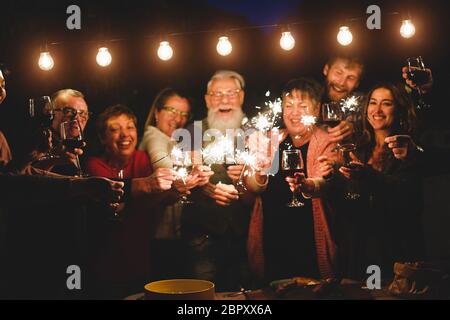 Glückliche Familie und Freunde feiern mit funkelnden Feuerwerk zu Hause Abendessen - verschiedene Alter der Menschen, die Spaß zusammen in Terrasse Party - Feier Stockfoto