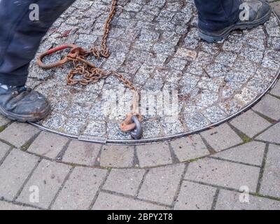 Unkenntlich städtischen Versorgungsarbeiter Eröffnung einer schweren doppelten Schachtabdeckung auf einer Straße mit Betonpflaster gepflastert Steine. Stockfoto