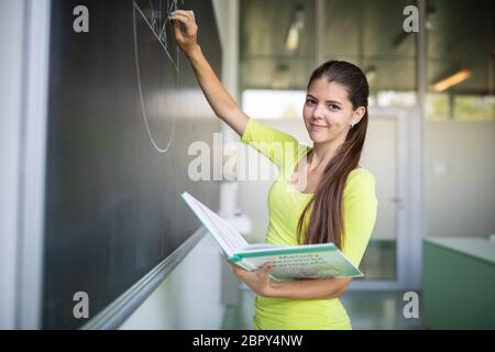 Weibliche Studentin vor einer Tafel, ein Problem zu lösen - junge Lehrer im Klassenzimmer eine Planimetry Problem auf der Tafel Stockfoto