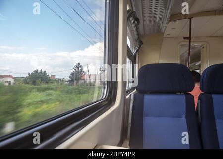 Leere Sitze in einem modernen Regionalzug, im europäischen Stil, auf einer Fahrt in einer Landschaft mit einem Geschwindigkeitsunschärfe-Effekt aus dem Fenster. Bild eines Typi Stockfoto