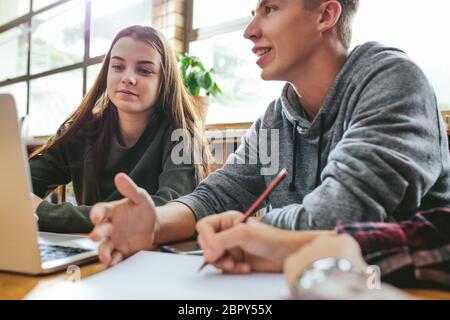 Studenten arbeiten an Schulprojekt in der Bibliothek, sitzen am Tisch mit Laptop und Bücher. Junge Studenten, die in der Bibliothek studieren. Stockfoto