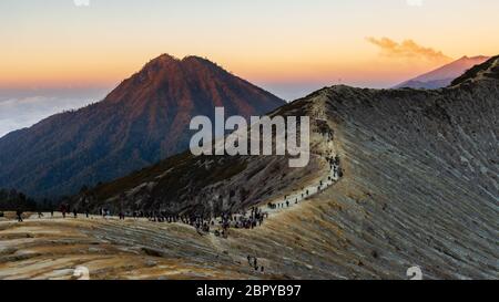 Menschen beobachten den Sonnenaufgang vom Kraterrand des aktiven Vulkans Ijen mit Hintergrundrauch. Stockfoto