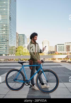 Side voller Länge Ansicht von schönen lächelnden Mann in formeller Kleidung auf der Terrasse mit Fahrrad mit Smartphone stehen Stockfoto