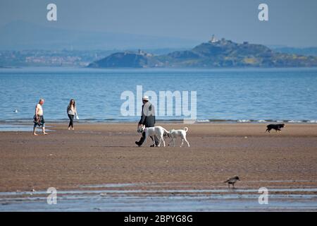 Portobello.Edinburgh, Schottland, Großbritannien. 20 Mai 2020. Ruhiger Start heiß sonnig und 18 Grad Celsius vor 10 Uhr. Hundespaziergänger, der mit zwei Passanten am Sandstrand entlang läuft. Stockfoto