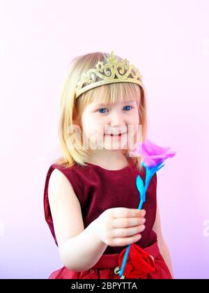 Kleine Mädchen in der Krone Blüte geben. Kleine Prinzessin mit rosa Blume. Nettes Mädchen mit Krone auf dem Kopf mit rosa Rose. Kind im schönen Kleid smilin Stockfoto