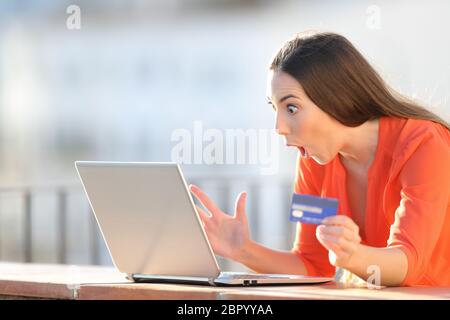 Erstaunt Käufer holding Kreditkarte finden online bietet auf dem Laptop in einen Balkon Stockfoto