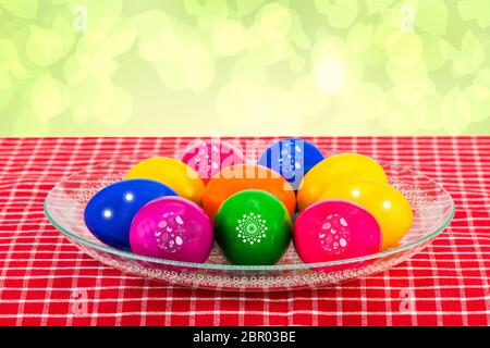 Ostern Dekorationen Hintergrund. Bunte ostereier in einer Glasschale auf einer rot karierten Tischdecke vor abstraktem hellgrünem Hintergrund. Religion an Stockfoto