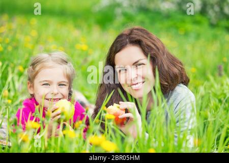 Mutter und Tochter liegen auf der grünen Wiese und Äpfel essen Stockfoto