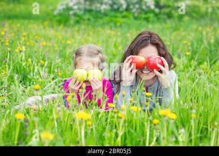 Mutter und Tochter auf grüner Wiese liegend und mit Äpfeln Stockfoto