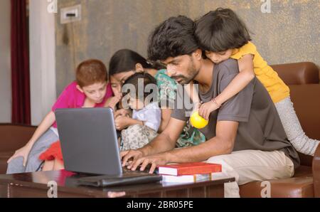 Kinder oder Kinder spielen, indem sie auf Vater zurück reiten und stören, während Vater beschäftigt in der Arbeit am Laptop - Konzept der Arbeit von zu Hause oder WFH während der covid Stockfoto
