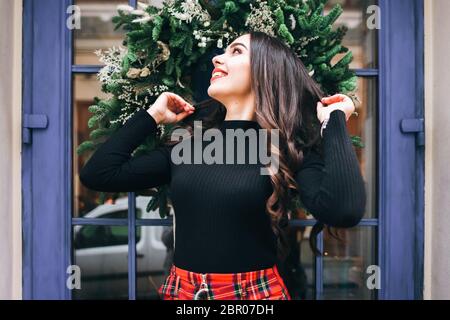 Nettes Mädchen Posen auf dem Hintergrund einer blauen Tür mit einem Weihnachtskranz für die Neujahrsferien dekoriert Stockfoto