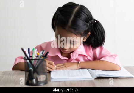 Das kleine Mädchen Hausaufgaben konzentriert zu. Kinder mit einem gelben Bleistift schreibt ein Notebook auf dem Holztisch. Wählen Sie Fokus geringen Tiefe von Fiel Stockfoto