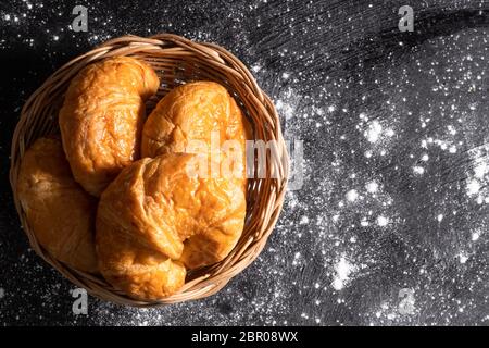 Von oben gesehen Croissants in einem Weidenkorb auf einem schwarzen Boden, die Gebäck Teig macht gelegt Stockfoto